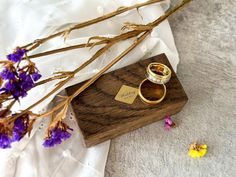 two wedding rings sitting on top of a wooden box next to dried flowers and petals