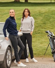 two women standing next to a car in front of a golf course with bags on the ground