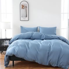 a bed with blue sheets and pillows in a white room next to a wooden floor