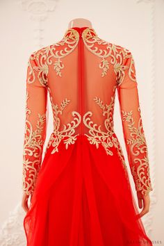 the back of a red dress with gold embroidery on it and an open neckline