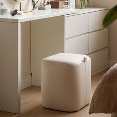 a white vanity with a mirror, stool and plant in the corner next to it