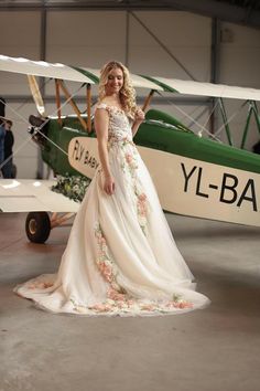 a woman in a wedding dress standing next to a small green and white plane with flowers on it