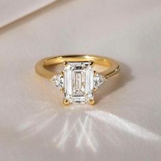 a gold ring with an emerald cut diamond in the center and three diamonds on each side