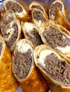 some meat and cheese rolls are in a tin foil container on a table with other food items