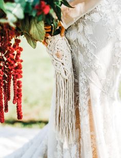 a woman in a white dress holding a bouquet of red flowers and greenery on her arm