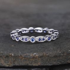 a white gold ring with blue sapphires and diamonds on top of a black rock