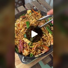 someone is holding a skillet full of noodles and vegetables with chopsticks in it