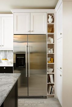 a stainless steel refrigerator in a white kitchen with marble counter tops and floor tiles on the walls