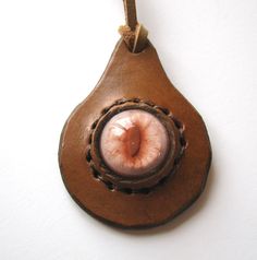 an eyeball hanging from a brown leather pendant on a white wall with a cord