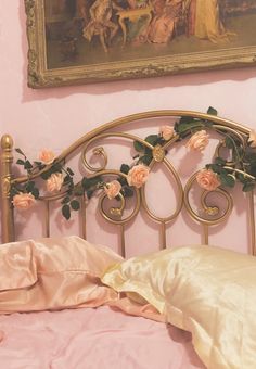 a bed with pink sheets and flowers on it next to a painting hanging above the headboard