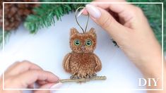 an owl ornament being held by someone's hand with pine cones in the background