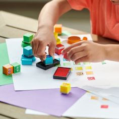 a child playing with blocks and shapes on a table in front of colored paper sheets