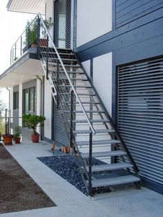 a set of metal stairs leading up to a white building with blue shutters on the side