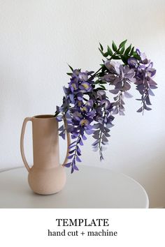 a vase with purple flowers sitting on top of a table next to a white wall