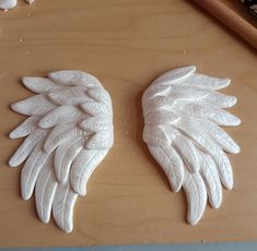 two white angel wings sitting on top of a wooden table next to a pair of scissors