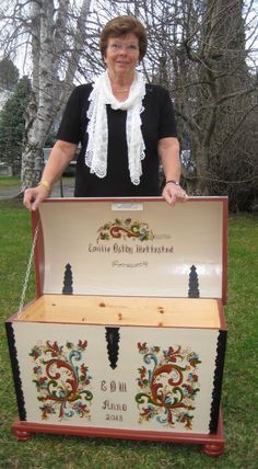 a woman standing next to an old trunk with embroidered designs on the front and sides