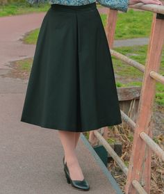 a woman standing on a wooden bridge wearing a skirt and blue blouse with floral print shirt