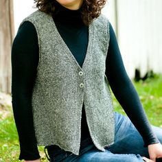 a woman sitting on the grass wearing a sweater vest