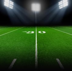 an empty football field at night with floodlights on the sidelines and green grass