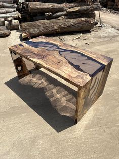 a wooden bench sitting on top of a sandy beach next to logs and trees in the background