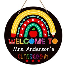 a welcome sign hanging from a rope with an apple and rainbow design on it's side