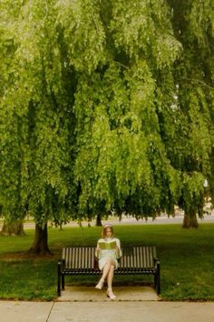 a woman sitting on a bench in front of a large green tree with lots of leaves