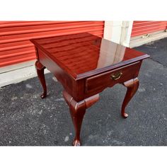 a small wooden table with drawers on the bottom and one drawer at the top, sitting in front of a red garage door