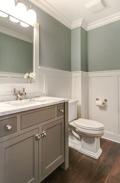 a white toilet sitting under a bathroom mirror next to a sink and wooden flooring