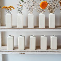 several white vases with orange flowers in them on a shelve shelf against a wall