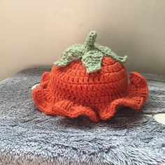 an orange crocheted hat sitting on top of a blue blanket next to a white wall