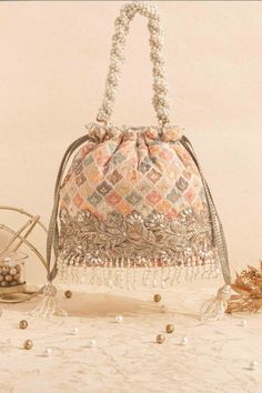 If unabashedly colour blocking is your go - to style, turn to our Aza bucket bag. The embroideries in pastel hues with a minimal hint of gold sequins and the rich pearl tassels are what makes it our favorite! Spice up your look with our Aza pastel bucket bag. Colour: Pastel Height: 7" (18 cm)  Base: 7.5" x 4.5" (19 cm x 11 cm) Handle drop: 5.5" (14 cm) Material: Banarasi organza silk, poly satin lining, pearl and crystal fringe lace, woven light gold thread drawstrings, braided pearl handle, pearl tassels. Pink Handwork Pouch Bag, Festive Multicolor Embroidered Potli Bag With Handwork, Festival Reception Potli Bag With Zari Work, Festive Multicolor Embroidered Handwork Potli Bag, Bollywood Style Bags With Handwork For Reception, Traditional Potli Bag With Dori Work For Reception, Zari Work Potli Bag For Festivals And Reception, Bollywood Style Handwork Bags For Reception, Traditional Festive Potli Bag For Reception