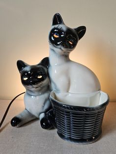 two black and white ceramic cats sitting next to each other in front of a lamp