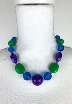 This is such a fun, colorful necklace! It has varying chunky plastic beads in green, blue, and purple and has gold toned metal findings. The clasp is a lobster claw clasp. The necklace measures 18.5 inches end to end. Era: 1980s Brand: LCI Size: 18.5 inches end to end Materials: Plastic or lucite beads, metal findings Country of Origin: Unknown Colors: Green, purple, blue Condition notes: Some scratches and general signs of use on the plastic beads. *This is a vintage item, therefore it is not i Multicolor Beaded Plastic Necklace, Playful Blue Beaded Necklace, Green Plastic Round Bead Jewelry, 80s Jewelry, Green Beaded Necklace, Purple And Green, Jewerly Diy, Colourful Necklace, Plastic Beads