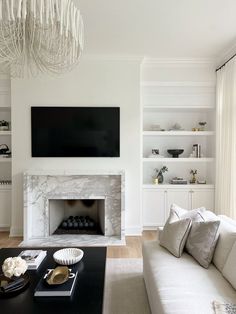 a living room with white furniture and a large tv mounted on the wall above a fireplace