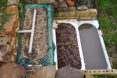 an old bathtub is filled with plants and straw next to a rock garden wall