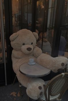 a large teddy bear sitting at a table with a coffee cup in its lap,