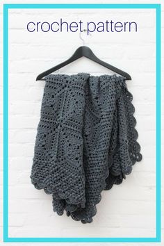 a gray crocheted shawl hanging on a white brick wall next to a black hanger