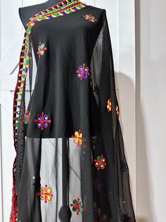 This black Navaratri dupatta features delicate thread work and glimmering mirrors, adding an elegant touch to any outfit. Made from georgette fabric, it is lightweight and comfortable to wear during festive occasions. Enhance your style and make a statement with this beautiful dupatta. Black Zari Work Blouse For Eid, Black Blouse Piece With Zari Work For Eid, Black Chanderi Blouse Piece With Traditional Drape, Black Embroidered Anarkali Saree, Festive Black Georgette Salwar Kameez, Black Semi-stitched Dupatta For Navratri, Unstitched Black Saree With Motifs, Black Chanderi Embroidered Saree Fabric, Black Georgette Salwar Kameez For Navratri