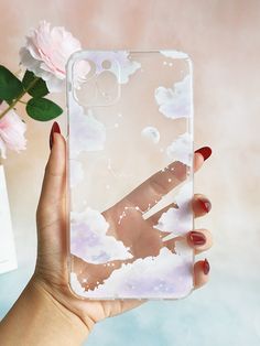 a hand holding up a clear phone case with clouds and stars on it, in front of a pink flower