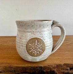 a coffee mug with a snowflake design on the side sitting on a wooden table