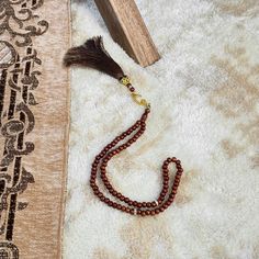 a tasseled beaded necklace laying on top of a white rug next to a piece of wood