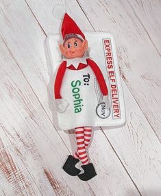 an elf doll is sitting on top of a white wooden floor with a sign that says,