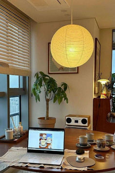 a laptop computer sitting on top of a wooden table in front of a lamp shade