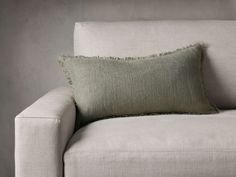 a white couch with a green pillow on it's back and a gray wall in the background