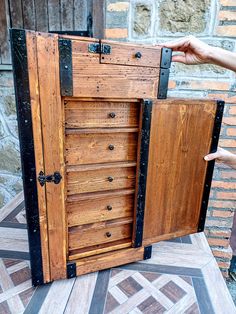 a person holding an open wooden chest on top of a tiled floor next to a brick wall