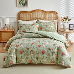 a bed with floral comforter and pillows in a room next to a lamp on a table