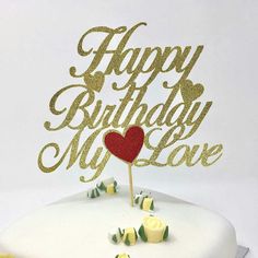 a white cake topped with a red heart and happy birthday cake topper next to yellow candies