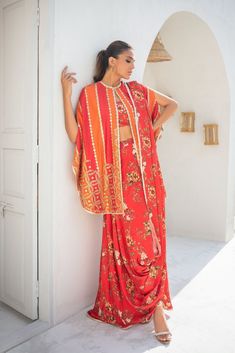 This worked bright coral pop khaddi silk cape is a sight for sore eyes. The inserts of bright vermillion with the printed vermillion charmeuse sari is styled and draped effortlessly to be cool and contemporary. Festival Saree With Dupatta And Cape Sleeves, Silk Dupatta With Cape Sleeves For Festivals, Festive Saree With Cape Sleeves, Bollywood Style Saree With Cape Sleeves For Festivals, Bohemian Red Pre-draped Saree For Festive Occasions, Festive Bohemian Draped Sets, Red Bohemian Saree With Sheer Dupatta, Traditional Cape-style Dupatta For Festive Occasions, Bohemian Draped Sets For Festive Occasions