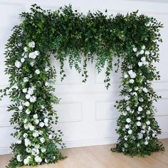 two white flowers and greenery are arranged in an arch