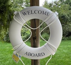 a life preserver with the words welcome aboard hanging on a pole in front of some grass